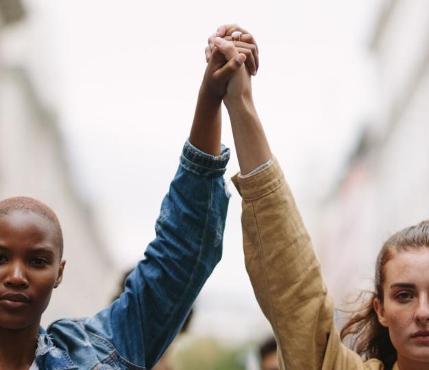 Two protestors holding hands aloft at a demonstration. 